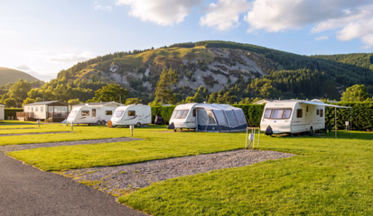 Touring caravans with awnings set up on grass pitches at the foot of a wooded hill