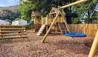 The play park, with a timber climbing frame, slide, cargo net and nest swing on bark chip