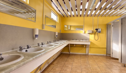 Washbasins along the tiled wall of the shower and toilet block, under a slatted ceiling