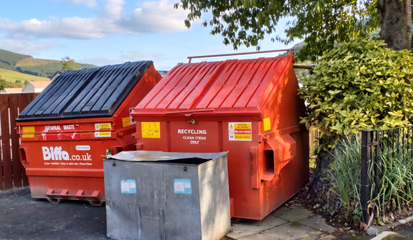 Red recycling and general waste bins at the waste point, with the hills behind