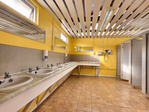 The shower and toilet block, with a row of washbasins along a tiled wall and cubicles beyond