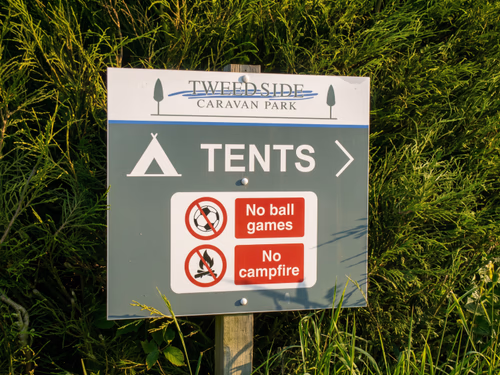 A site sign pointing the way to the tents field, with no ball games and no campfire notices below