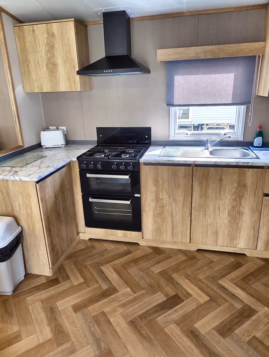 The kitchen of a hire caravan, with a gas cooker, extractor hood and sink under the window