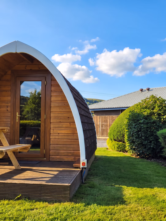 A timber camping pod with its curved roof against a blue summer sky